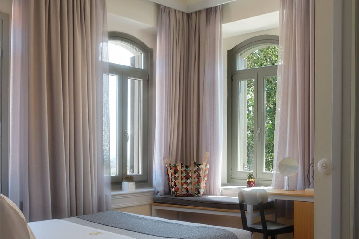 Ein Hotelzimmer mit Bett, Schreibtisch, Stuhl und einem fenster mit Vorhängen.
