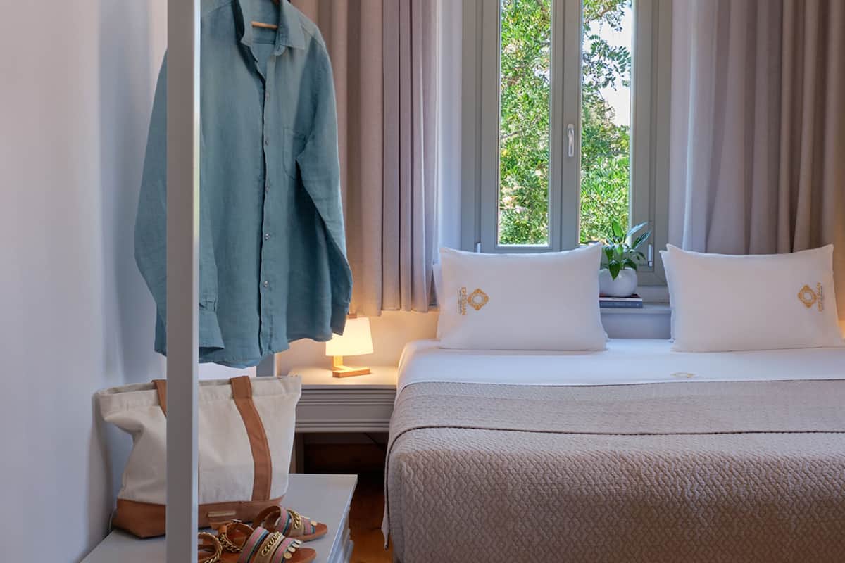 Ein Schlafzimmer mit Bett, Nachttisch, Kommode, Spiegel und einem fenster mit Vorhängen.