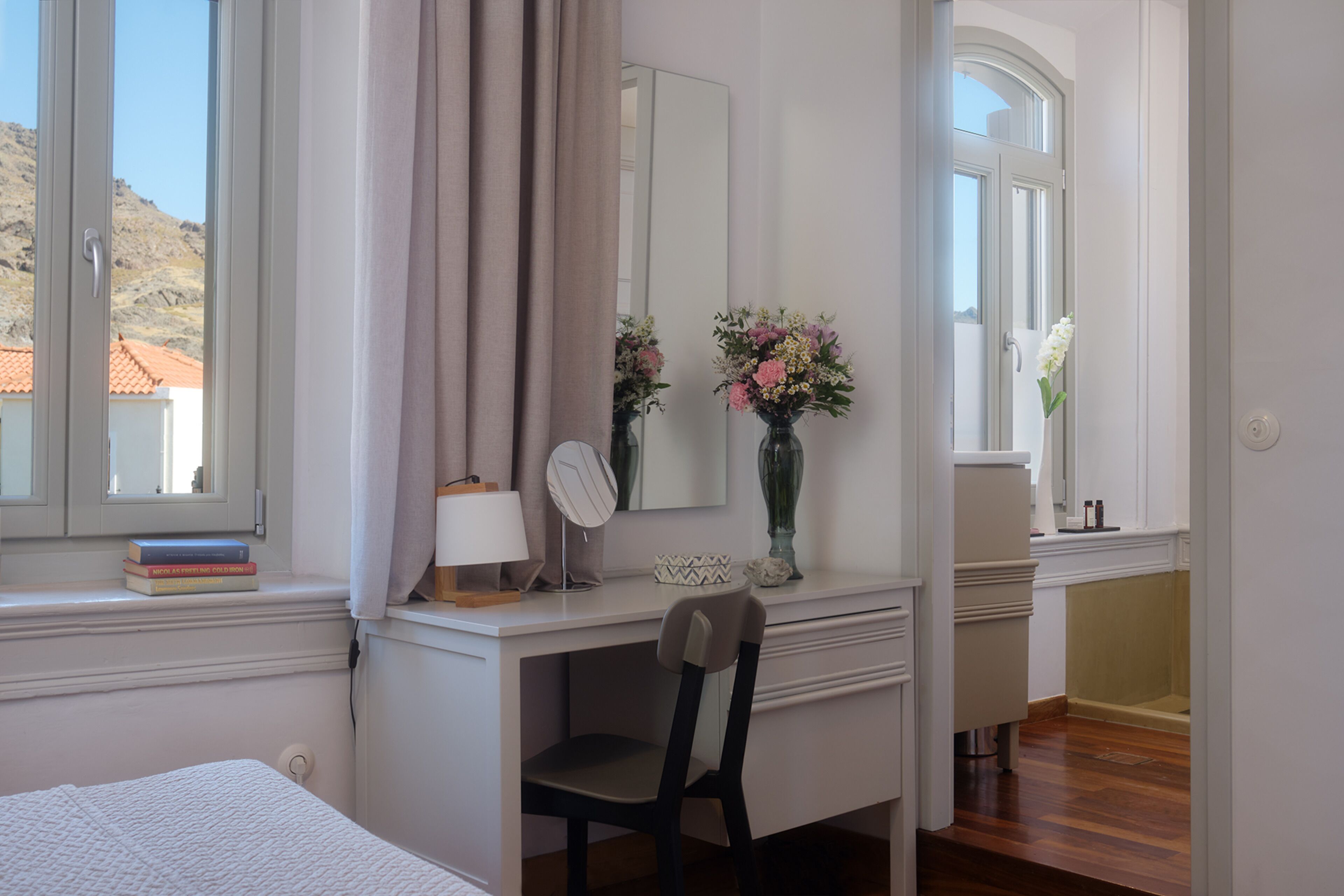 Une chambre à coucher avec un lit, un bureau et une chaise, un miroir et une fenêtre avec des rideaux.