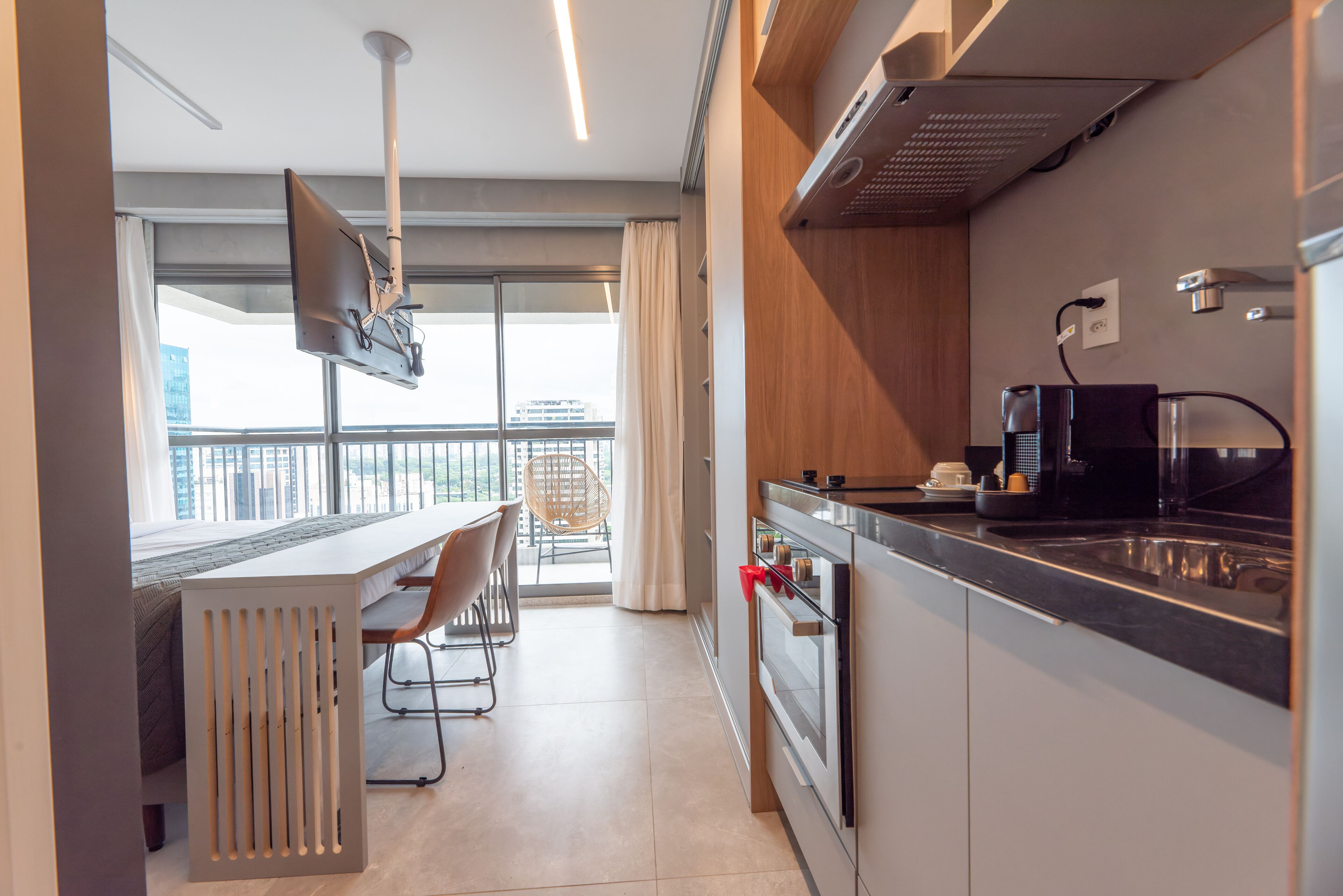 A modern kitchen with a built-in oven, a coffee maker, and a large window overlooking a balcony.