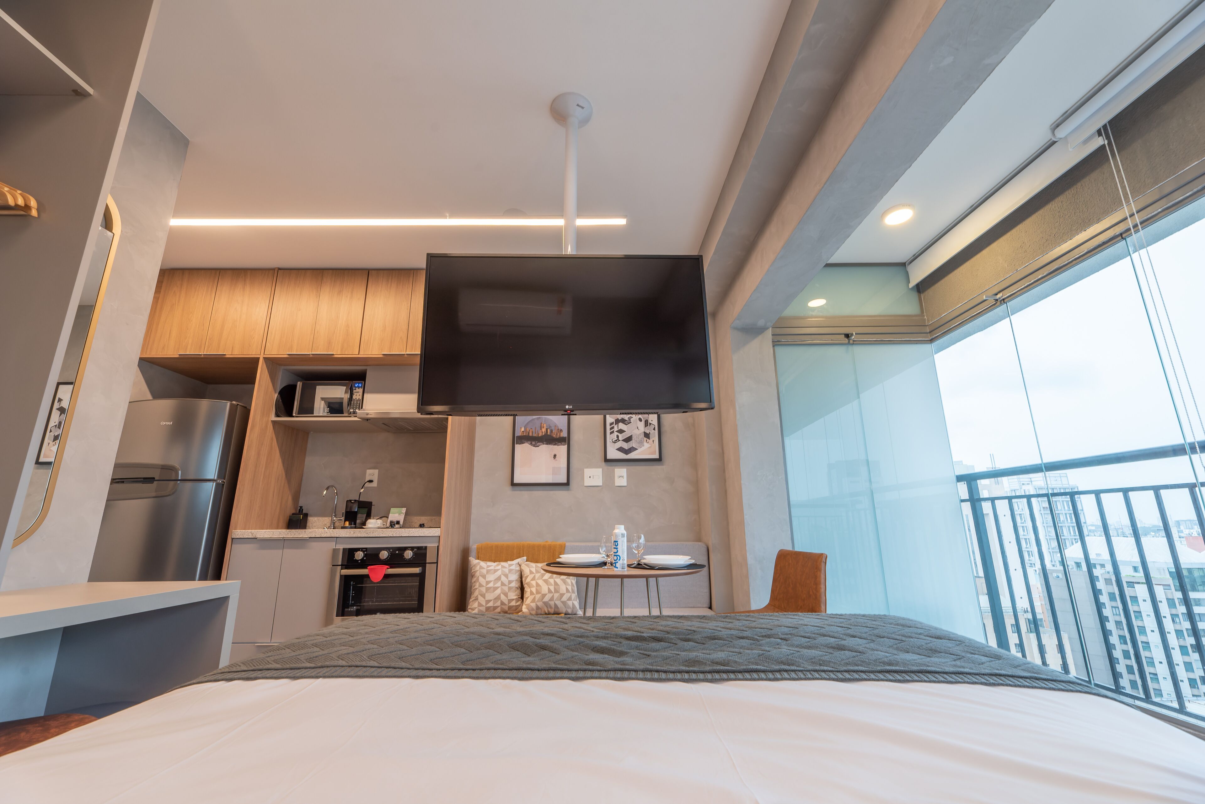 Een moderne hotelkamer met een bed, een kitchenette, een flatscreen televisie en een balkon met uitzicht op de stad.