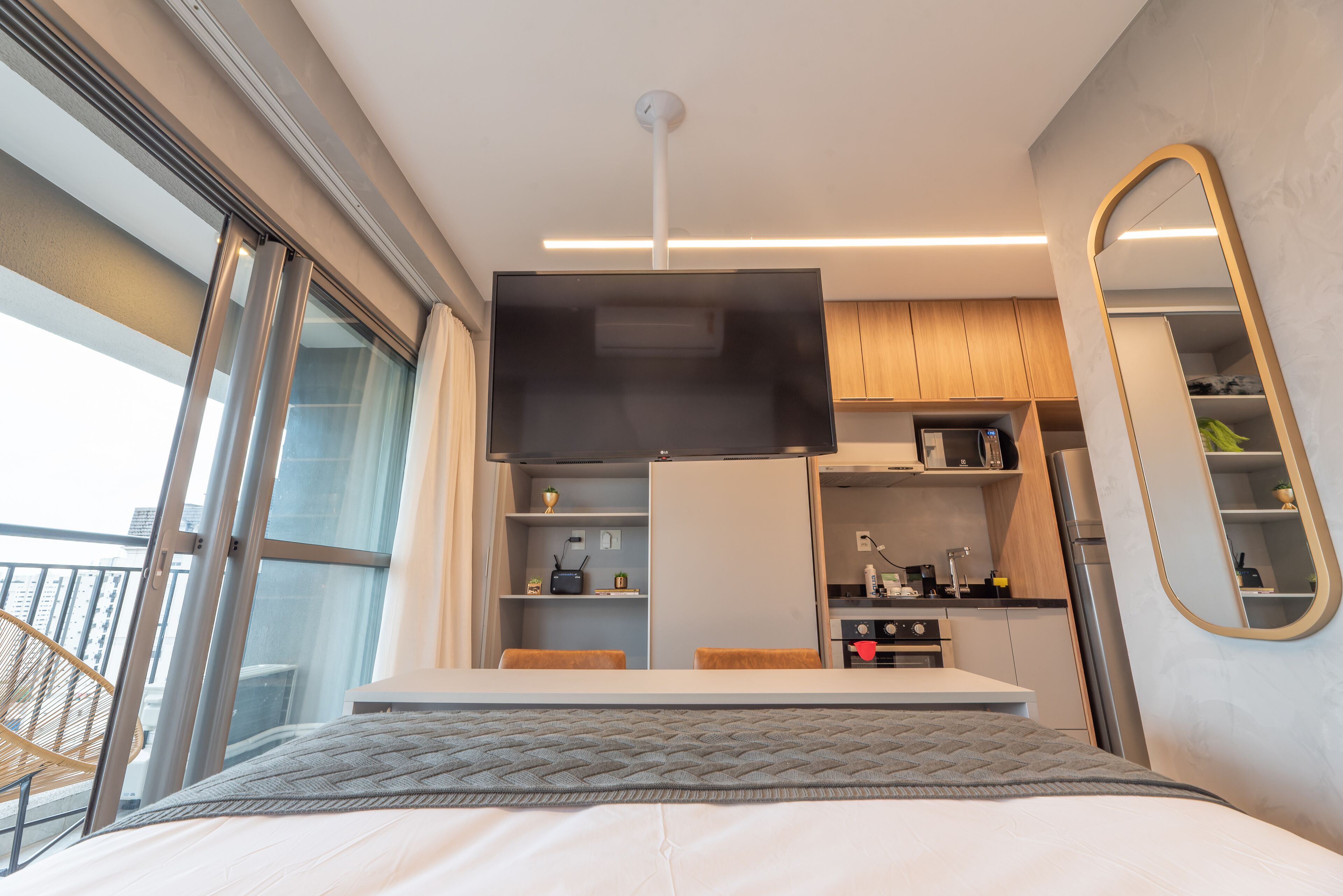 A modern bedroom with a large bed, a built-in desk, a kitchenette, and a balcony with a view.