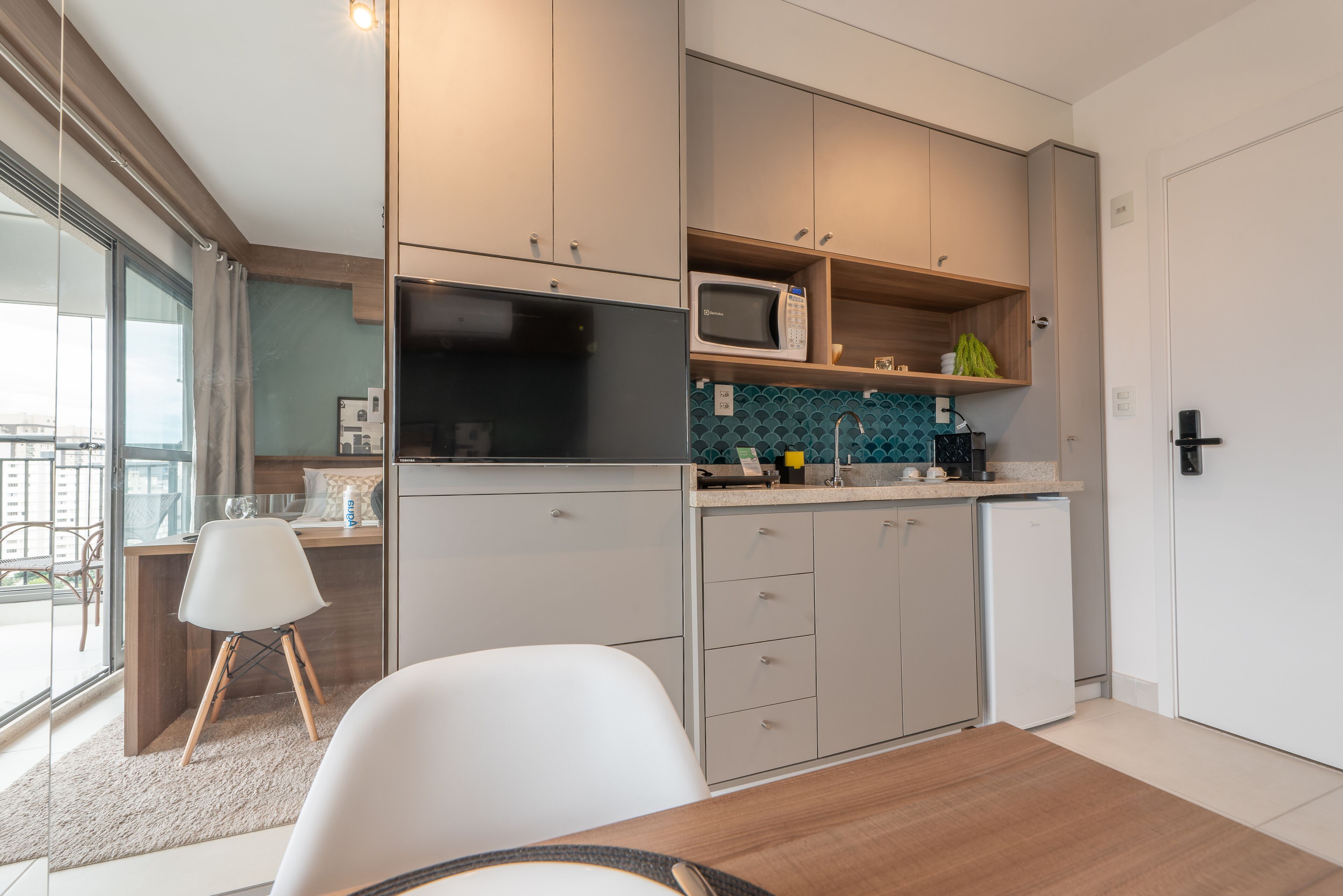 A modern kitchen with a built-in microwave, a coffee machine, and a small refrigerator. There is a dining area with a table and chairs.