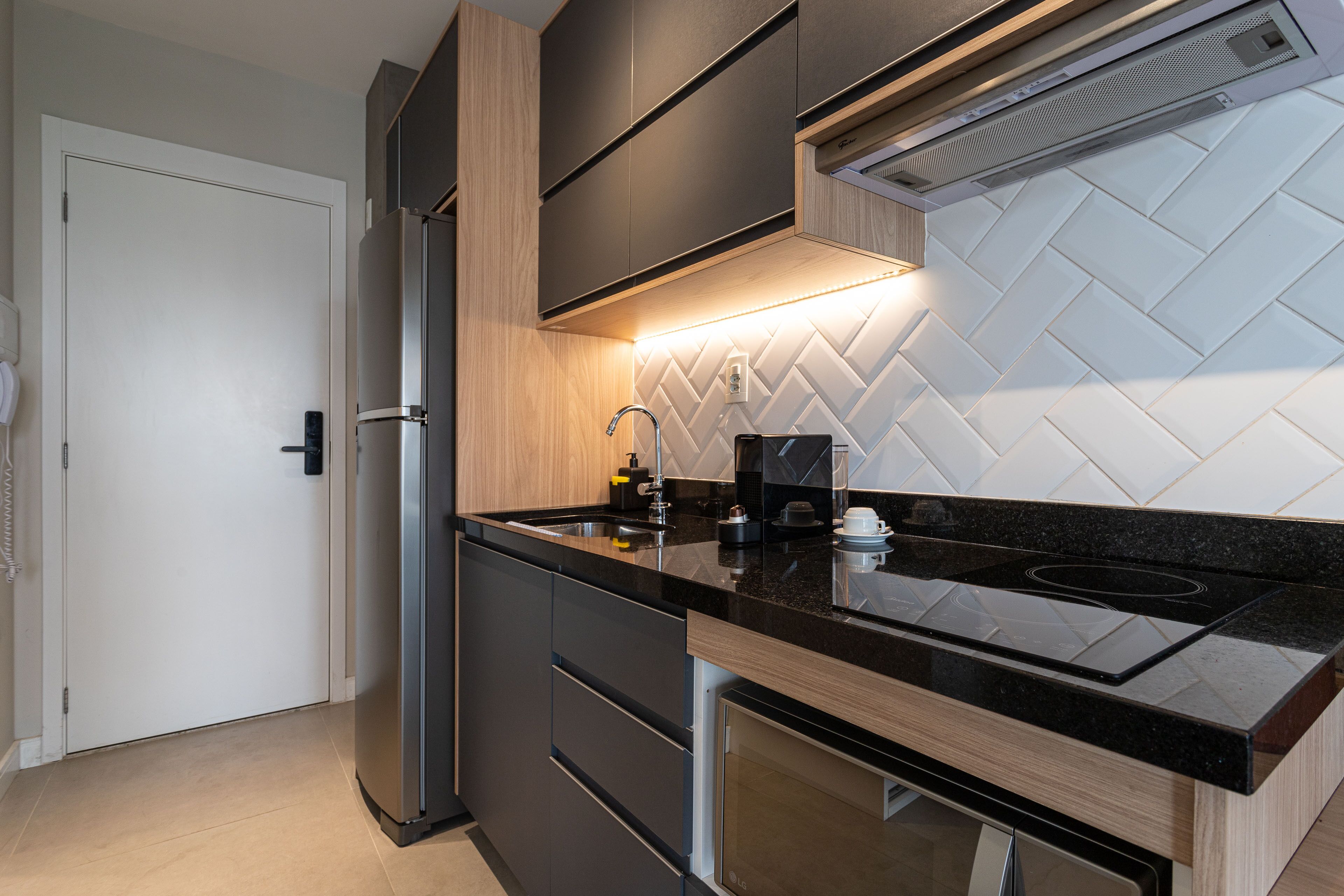 A modern kitchen with a stainless steel refrigerator, black countertop, and a herringbone-patterned backsplash.