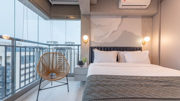 Een moderne hotelkamer met een groot bed, uitzicht op de stad, een wandairconditioner en een stoel bij het raam.