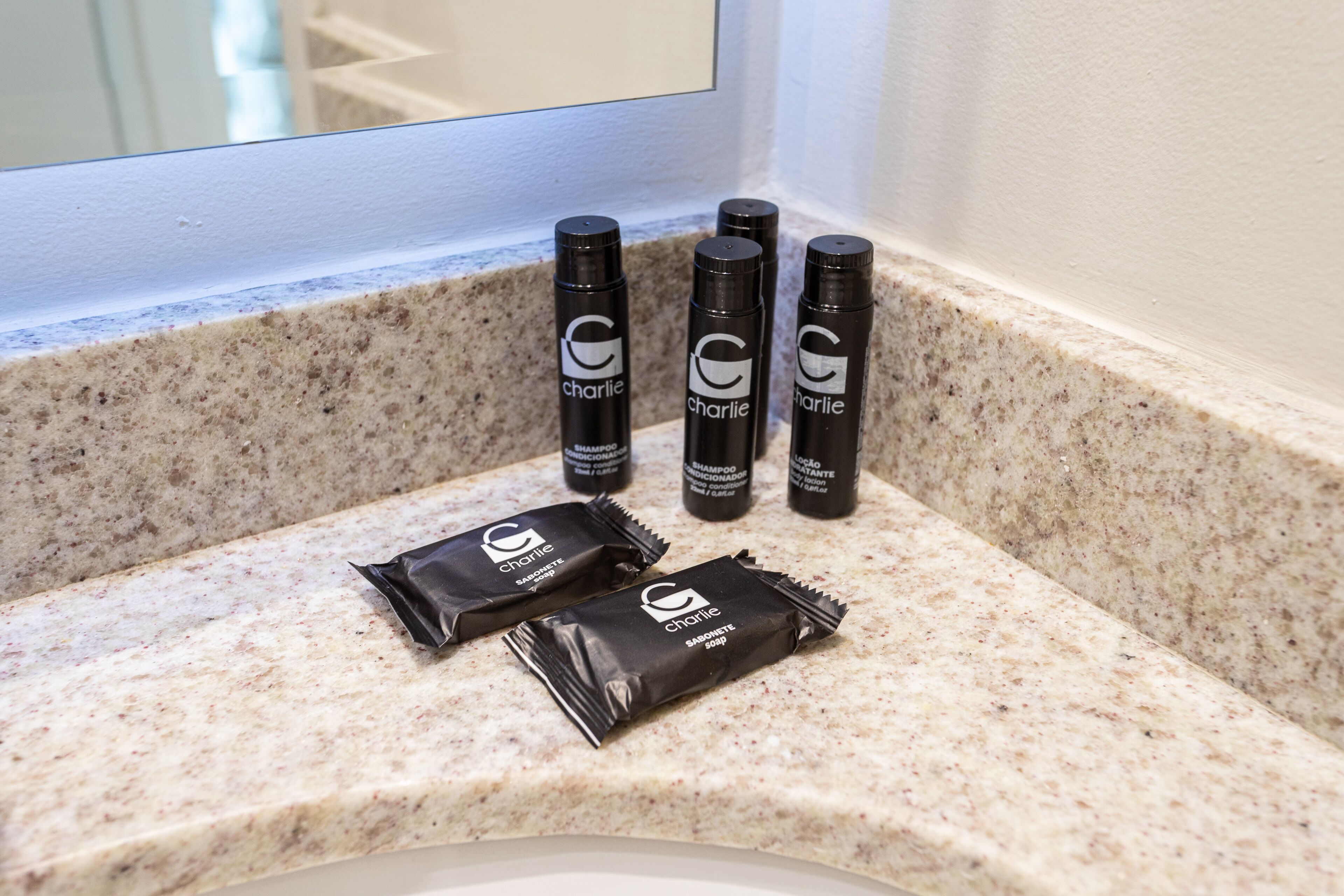 A bathroom counter with four bottles of Charlie shampoo and two packets of Charlie soap.