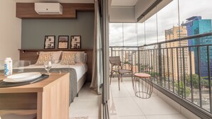 Een moderne slaapkamer met een bed, nachtkastje en een balkon met uitzicht op de stad.