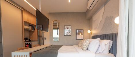 A modern bedroom with a bed, bedside table, and a small kitchenette area.