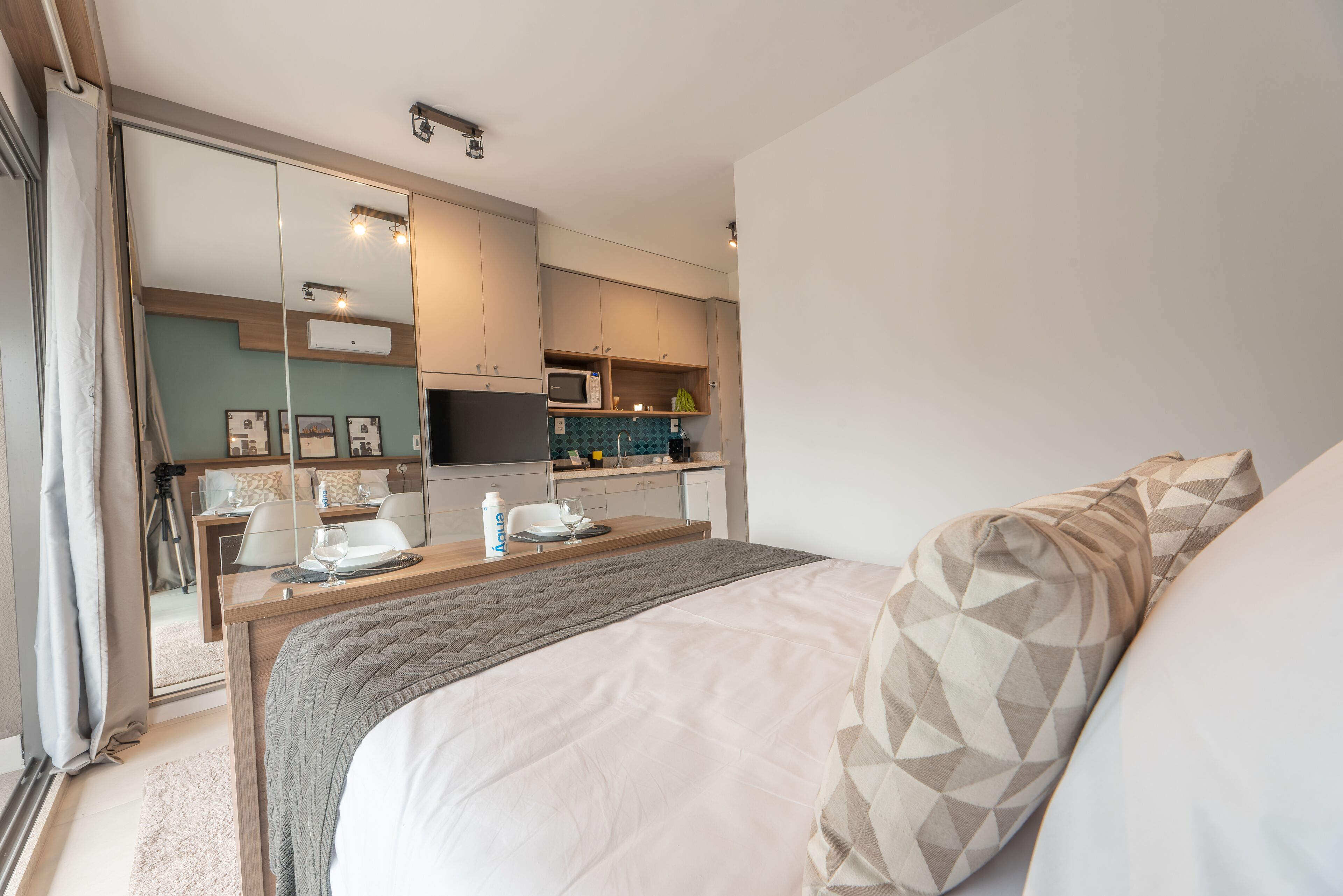 Een moderne hotelkamer met een groot bed, een nachtkastje, een bureau met stoel, een kitchenette en een schuifdeur naar een balkon.