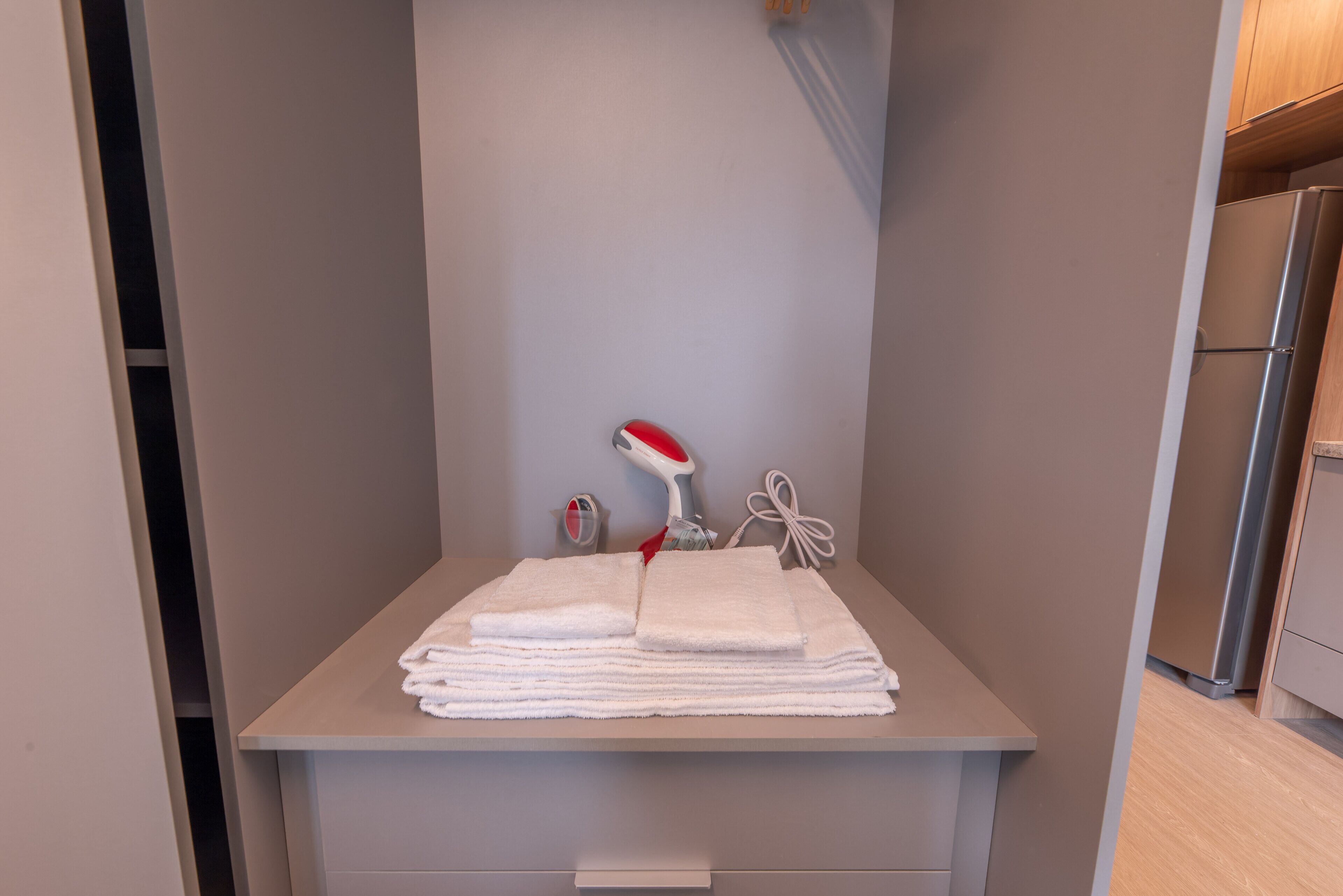 A bathroom with a towel rack holding several folded towels, a red and white hairdryer, and a small bottle.