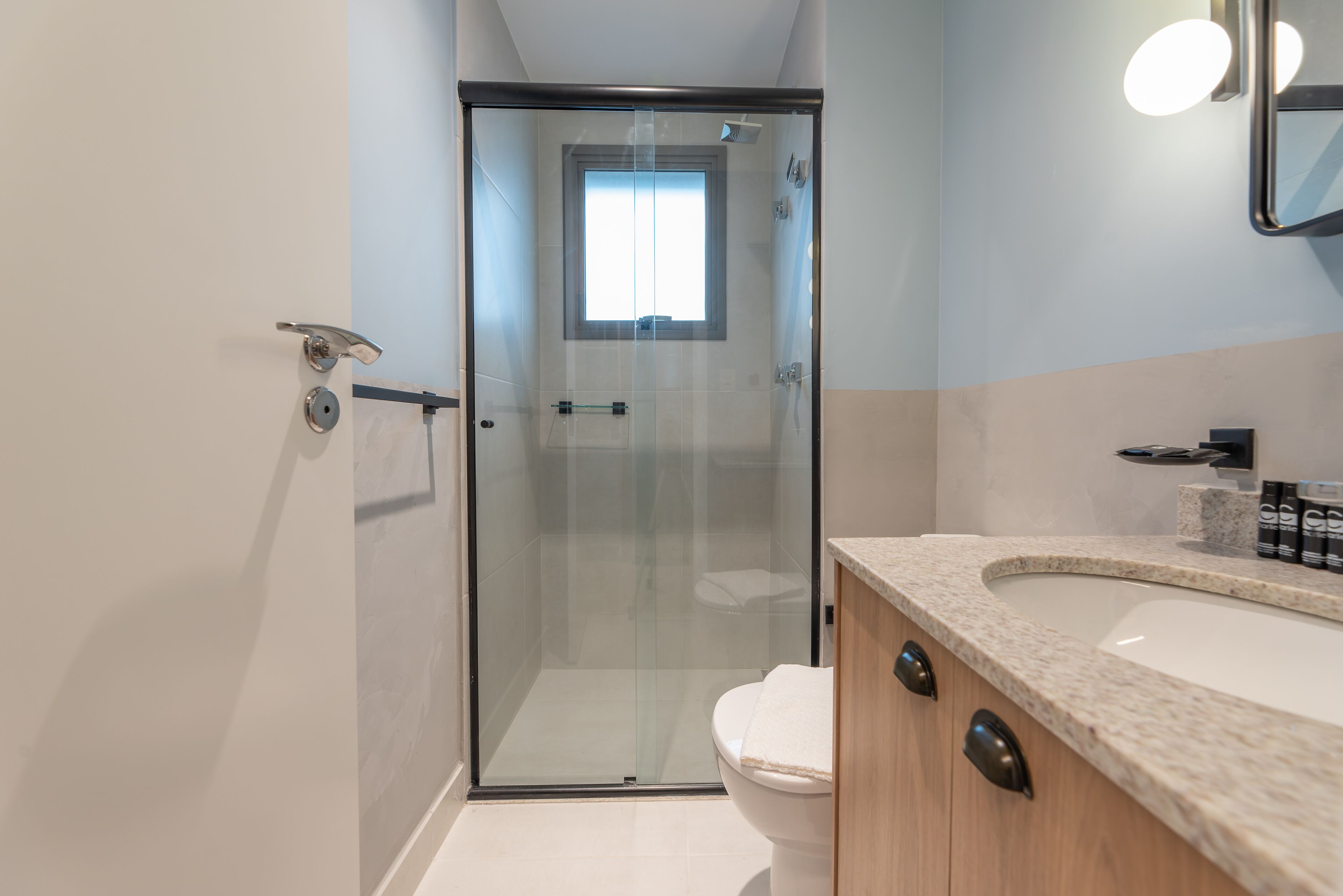 A modern bathroom with a glass-enclosed shower, a white toilet, and a granite countertop sink.