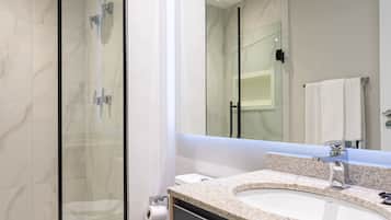 Un bany modern amb dutxa protegida per vidre, vàter blanc i un gran mirall sobre un lavabo amb encimera de granat.