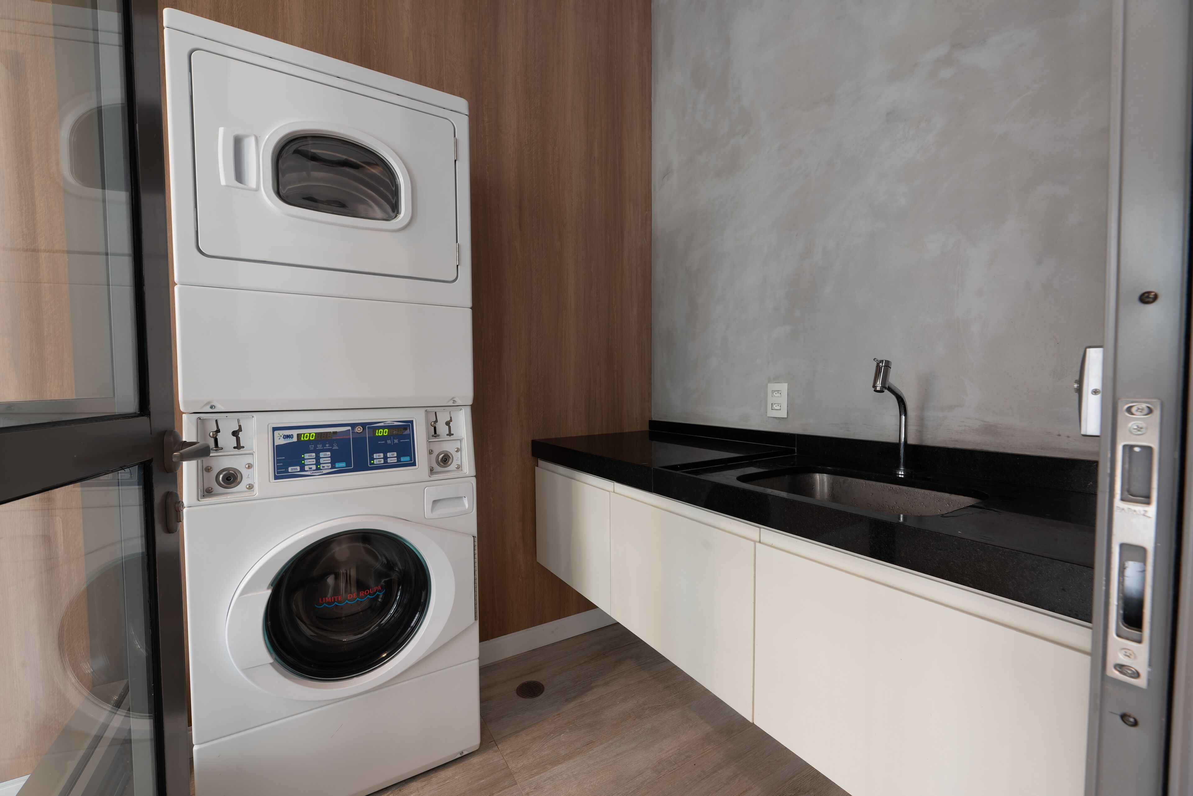 A compact laundry area with a front-loading washer and dryer, a black countertop, and a sink.
