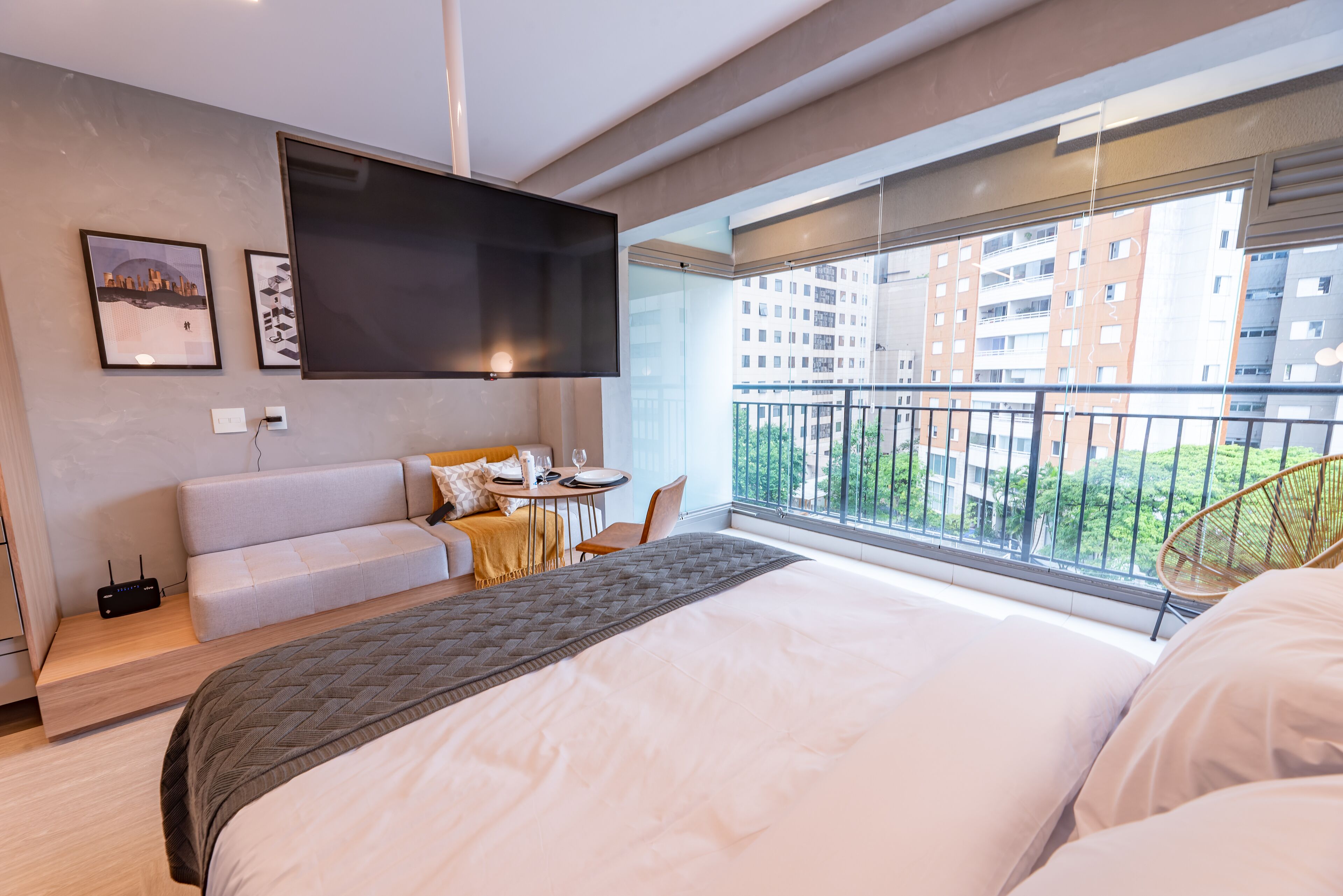Een moderne hotelkamer met een groot bed, een flatscreen televisie aan de muur, een balkon met uitzicht op de stad en een klein zithoekje.