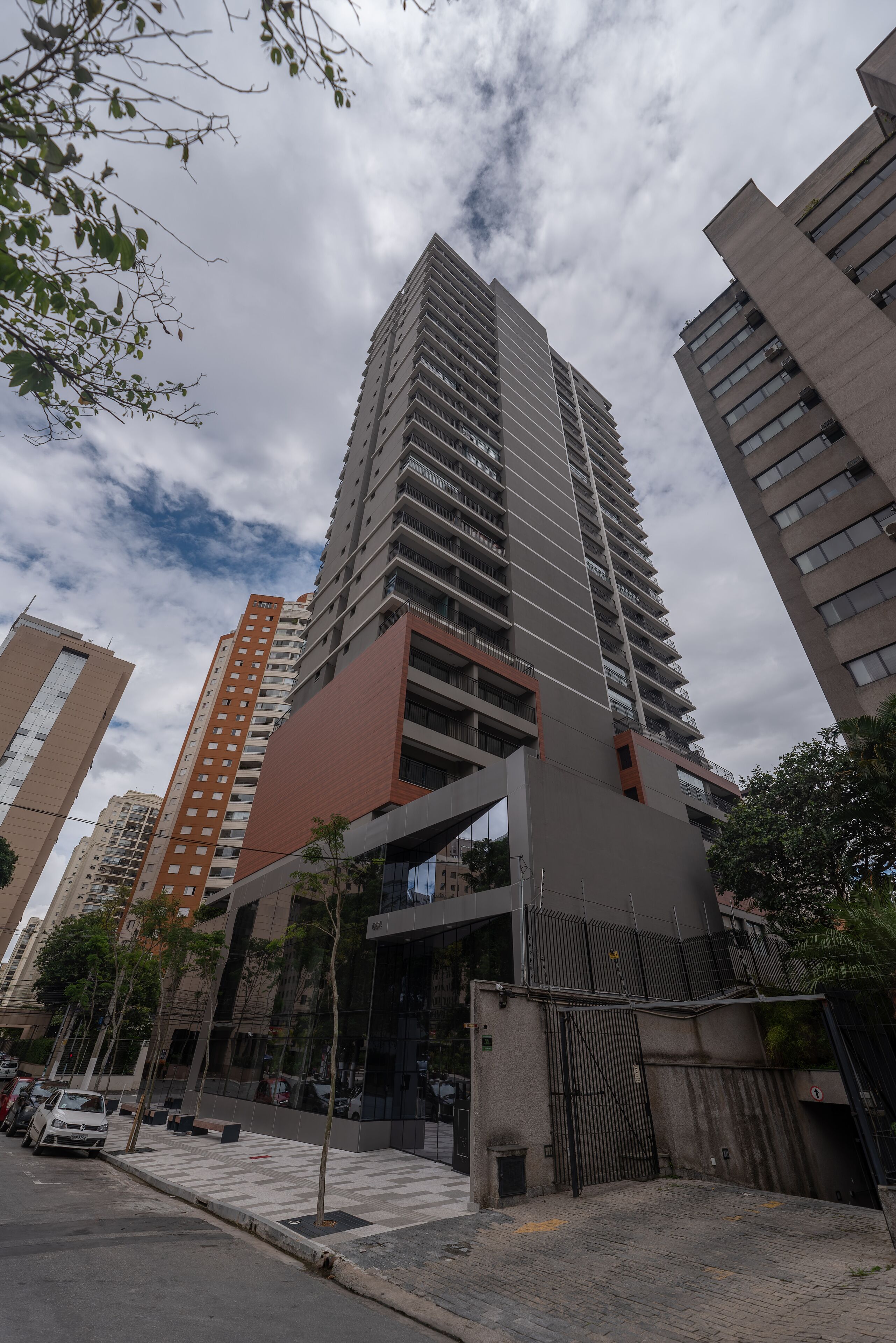 A high-rise building with multiple floors, a gated entrance, and a parking area with cars.