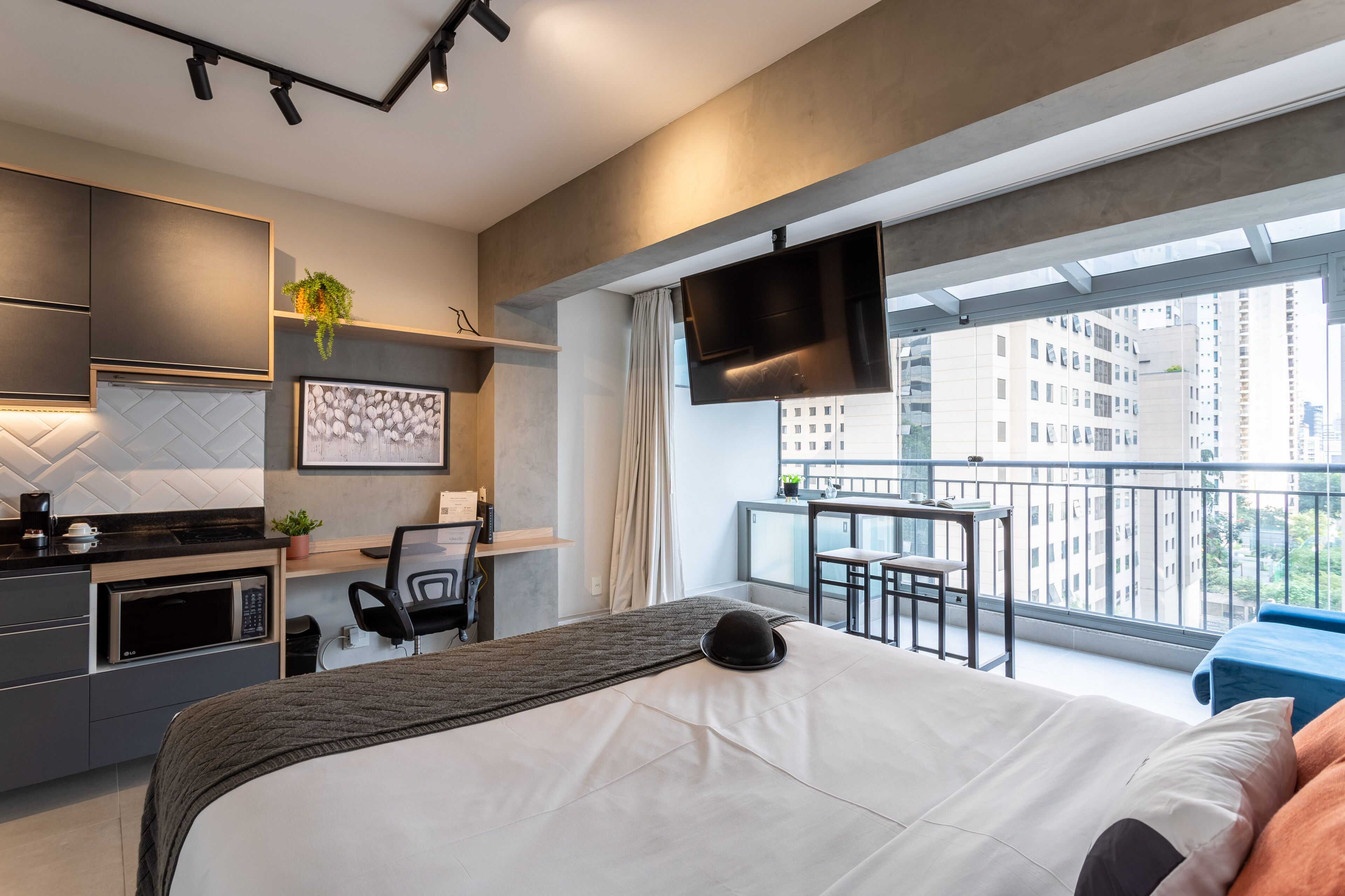 A modern hotel room with a large bed, a desk, a microwave, and a TV mounted on the wall.