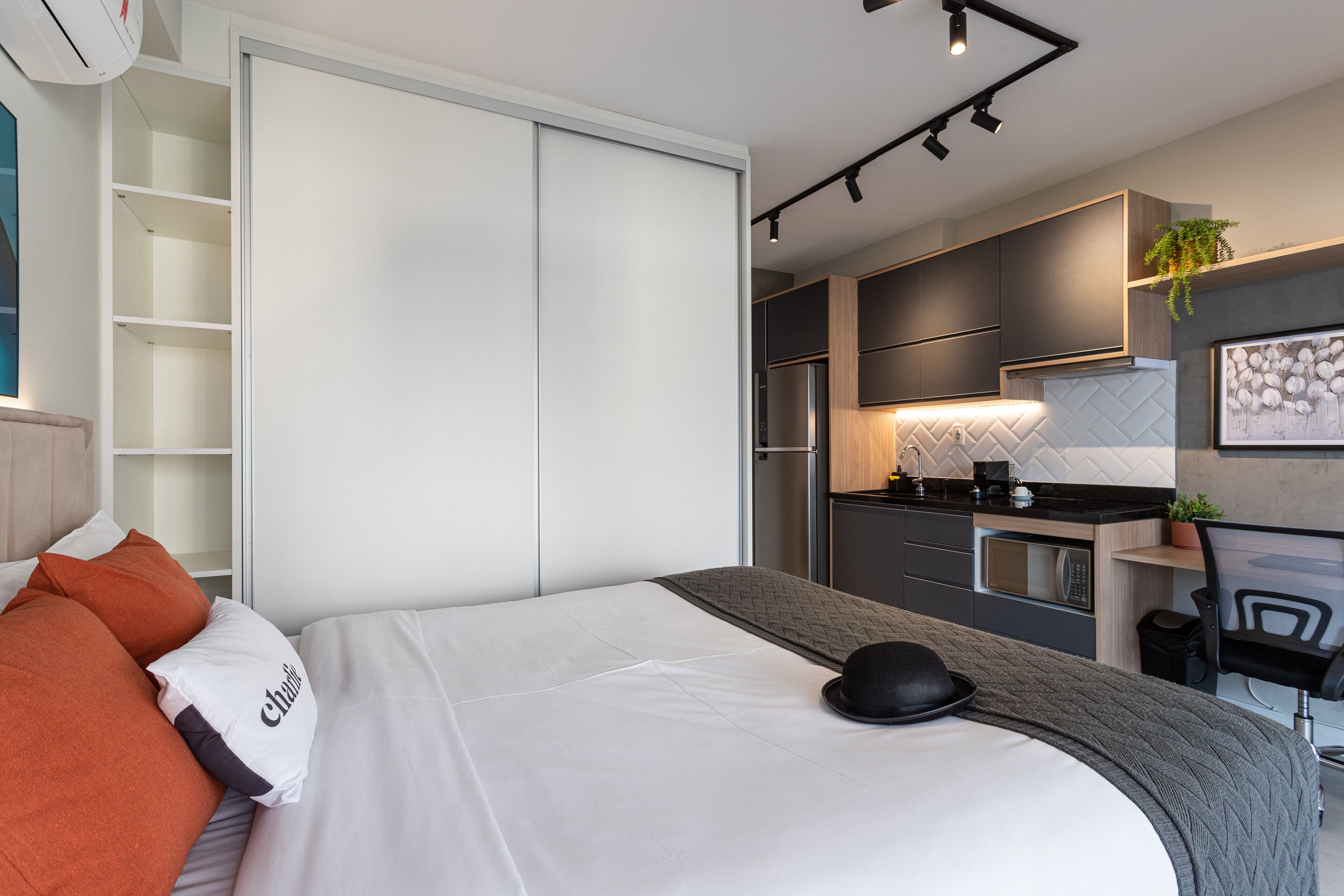 A modern hotel room with a bed, a desk, and a kitchenette.