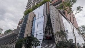 Een hoog, modern gebouw met een glazen gevel die reflecteert en een geometrisch grondvorm.