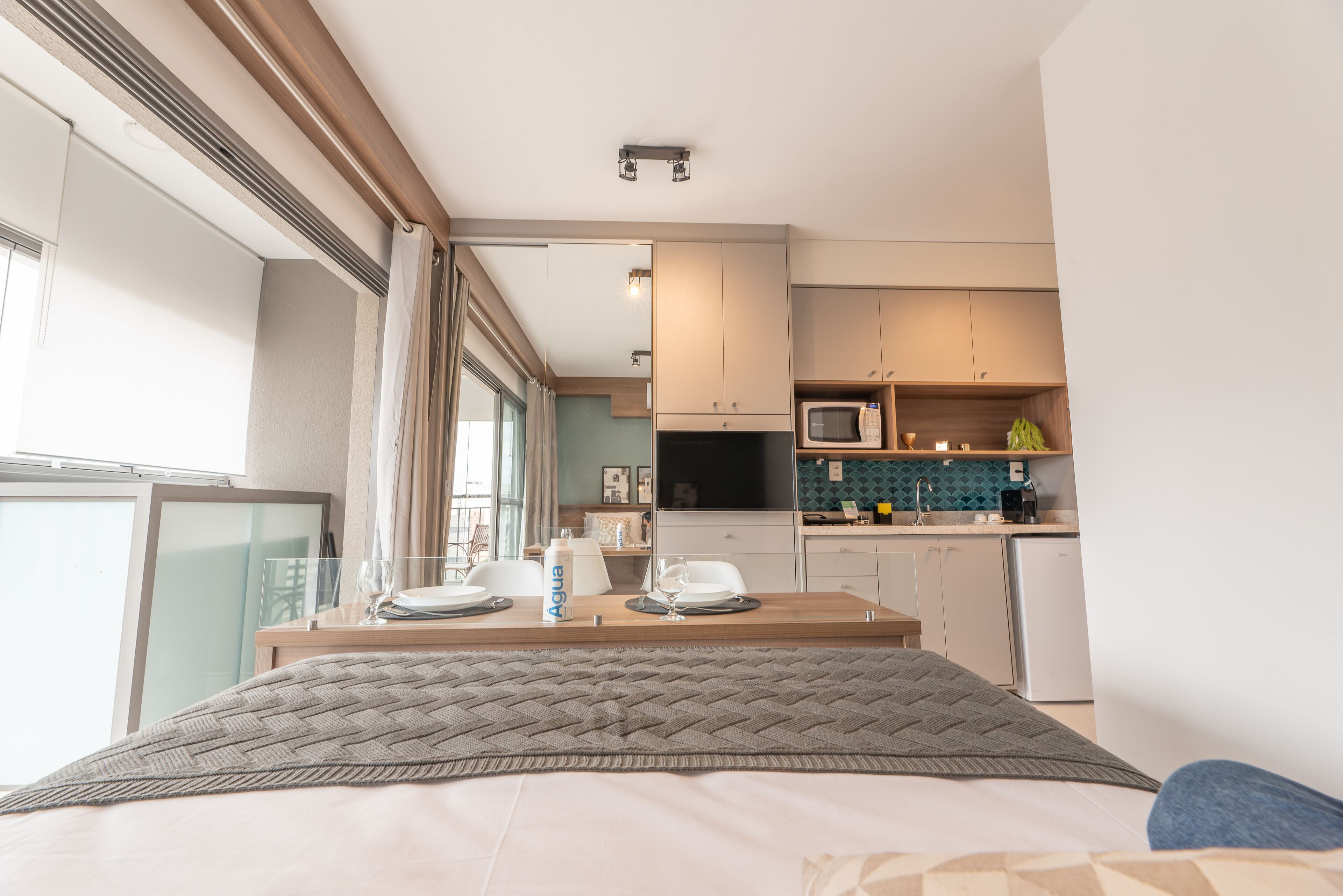 Ein modernes Hotelzimmer mit einem Bett, einer Essecke mit Tisch für zwei Personen, einer Küchenzeile und Blick auf die Stadt.