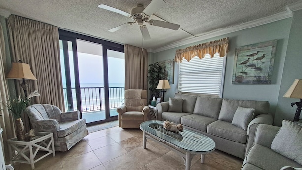 A spacious living room with a large window offering a view of the ocean, a ceiling fan, and a comfortable seating area with a sofa and armchairs. - Oceanfront Corner Three Bedroom Unit - Crescent Sands L5 (North Myrtle Beach)