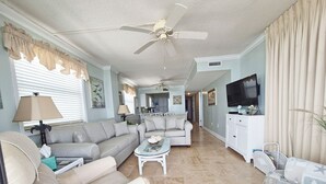 A spacious living room with a ceiling fan, a sofa, a coffee table, and a television. - Oceanfront Corner Three Bedroom Unit - Crescent Sands L5 (North Myrtle Beach)
