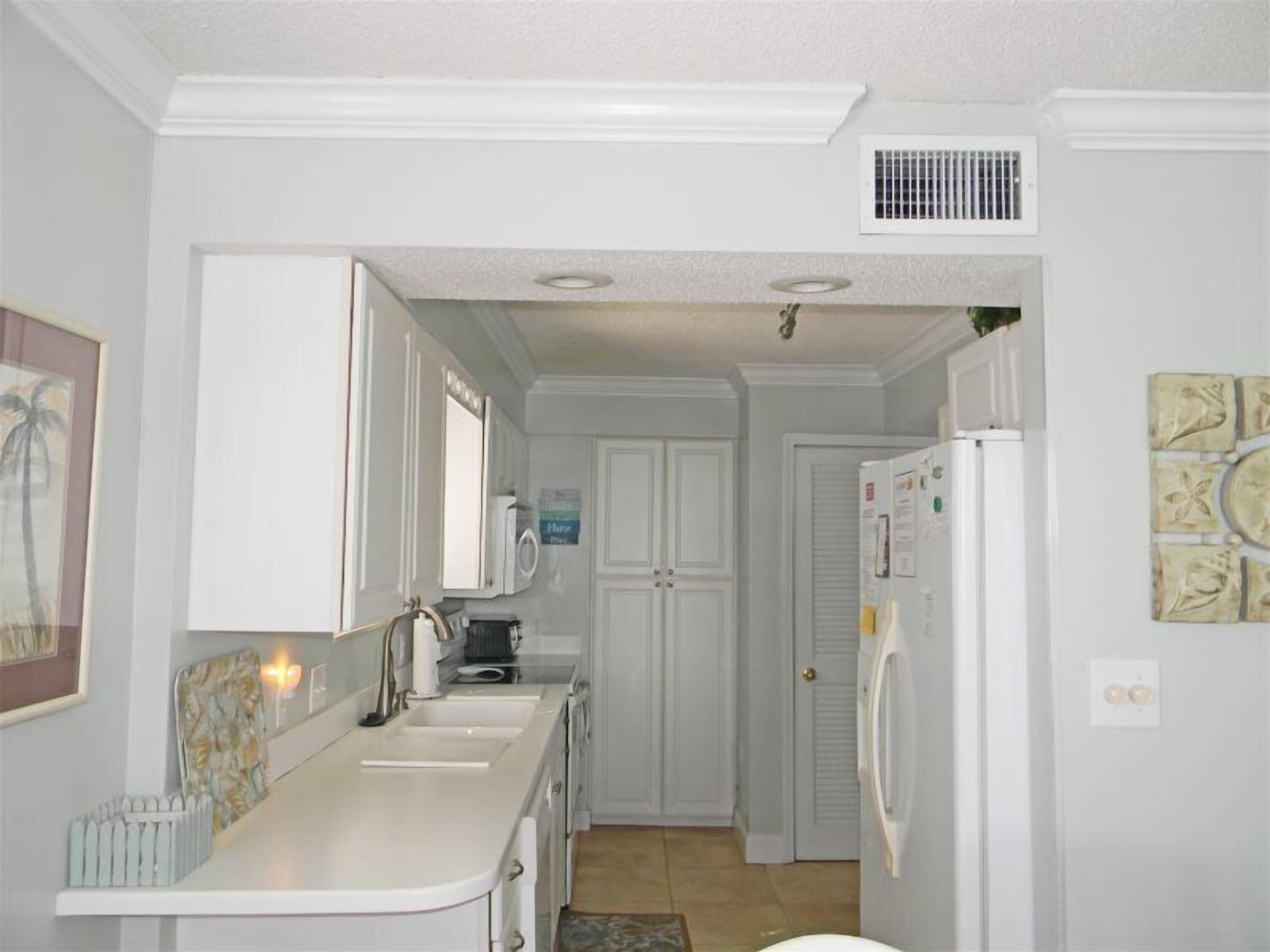 A kitchen with white cabinets, a microwave, a refrigerator, and a sink.