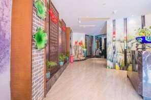 Un hall d’hôtel avec un mur en briques, des plantes en pot et un comptoir d’accueil en marbre.