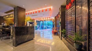 Vestíbulo de hotel con un mostrador de recepción de mármol, una escalera que conduce al piso superior y una pared decorativa con faroles rojos.