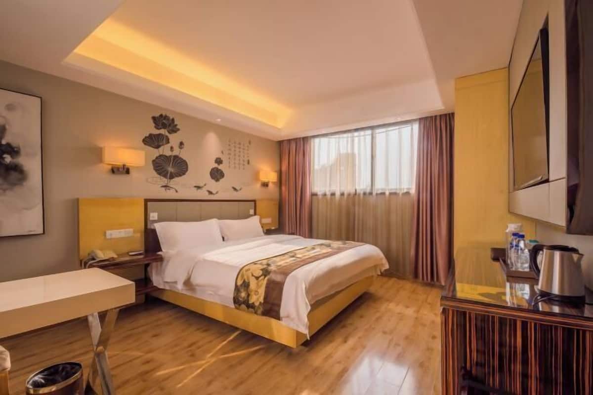 A hotel room with a bed, bedside table, lamp, and a large window with curtains.