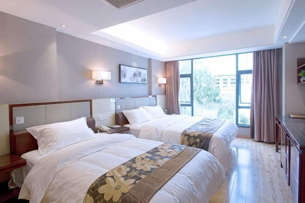 A hotel room with two beds, a nightstand, a desk, and a large window with curtains.