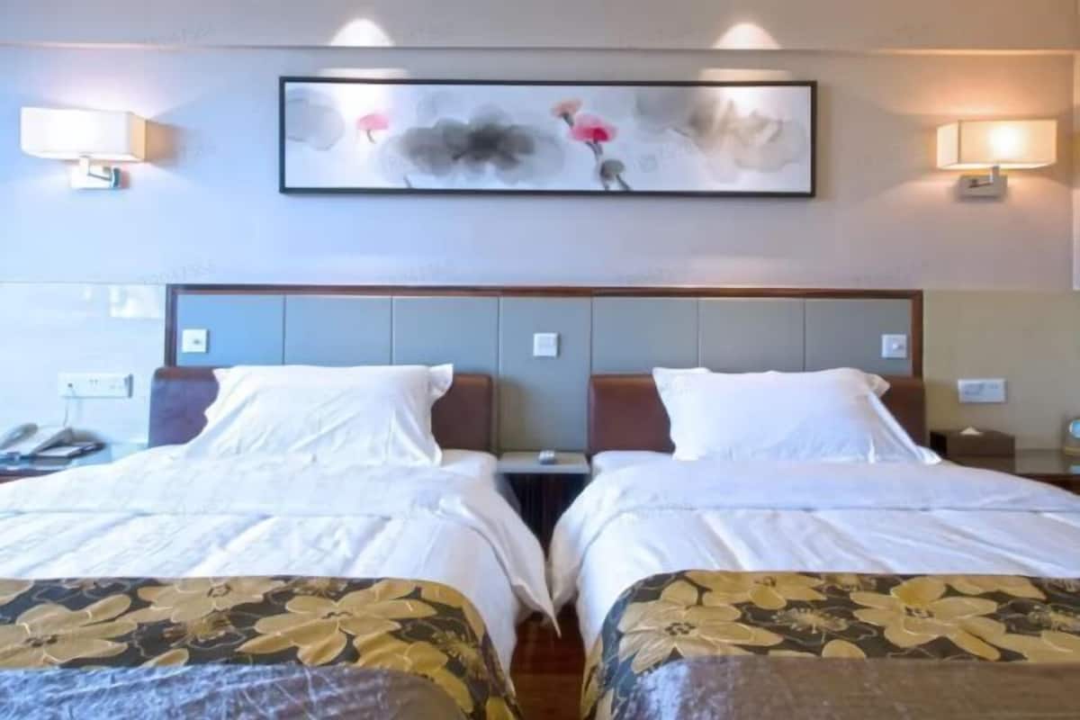 A hotel room with two beds, a painting on the wall, and bedside lamps.