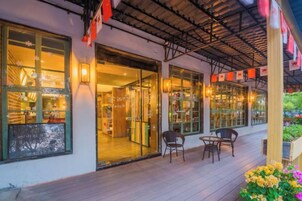 Un espacio al aire libre con techo, sillas y mesas, un escaparate con puertas de cristal y una terraza de madera.