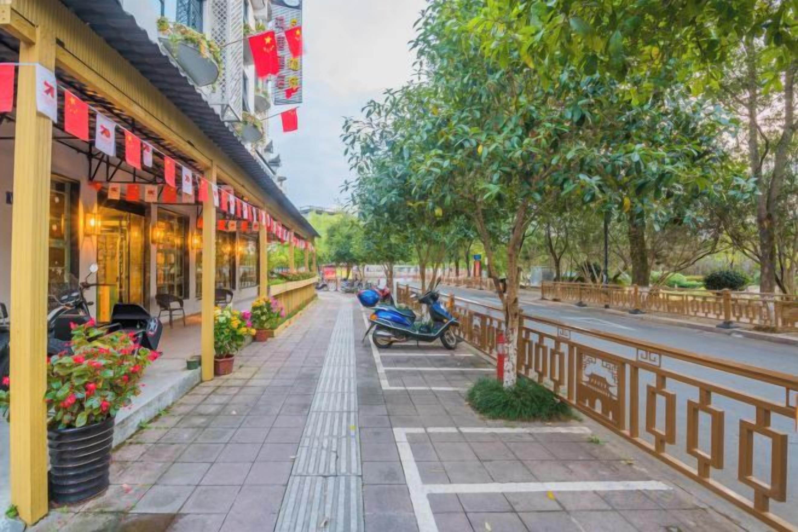 Una acera con un restaurante a la izquierda, un scooter azul y una calle arbolada.