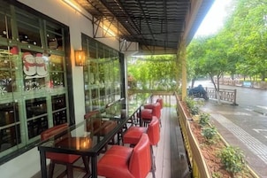 An outdoor seating area with tables and chairs, a glass enclosure with bottles, and a view of a street with trees.