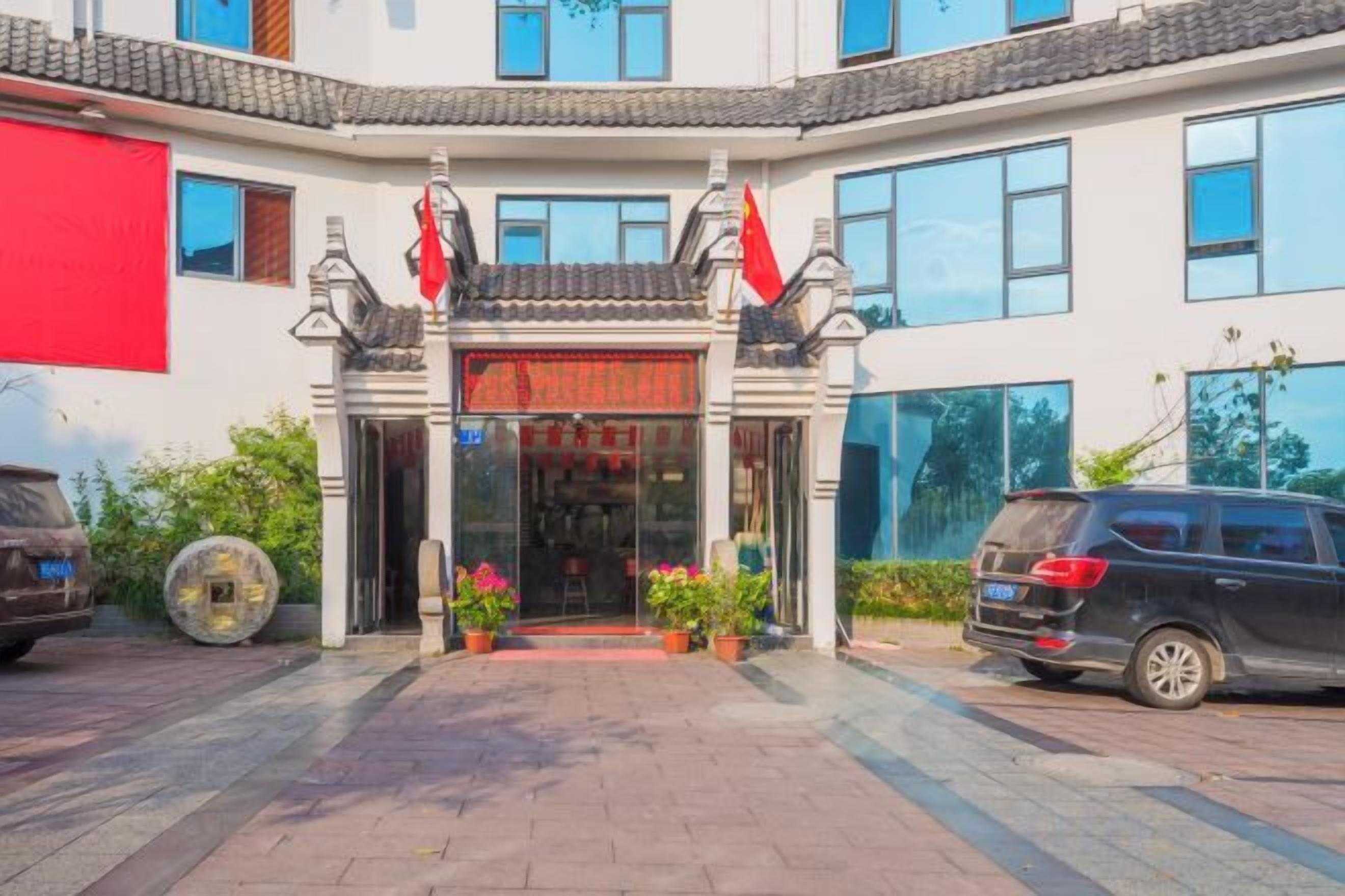 Un edificio con una entrada de arquitectura tradicional, un coche aparcado delante y un cartel rojo sobre la entrada.