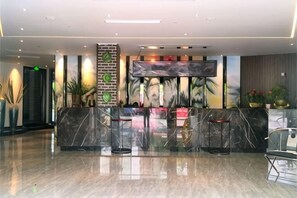 Zona de recepción de un hotel con un mostrador de mármol, un televisor de pantalla plana y plantas en macetas.