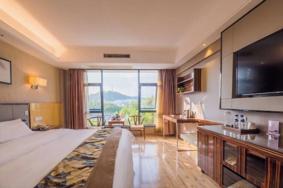 A hotel room with a bed, a desk, a TV, and a view of the outdoors.