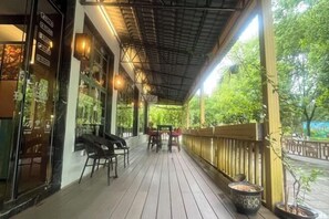 A covered outdoor seating area with tables and chairs, a wooden railing, and potted plants.