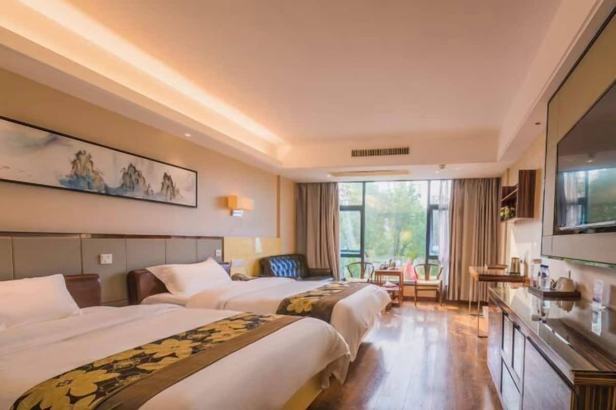 A hotel room with two beds, a desk, a chair, and a TV.
