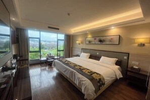 A hotel room with a large bed, a desk, a chair, a TV, and a view of the city. - Hantang Hotel (Taining)