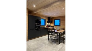 A modern kitchen with black cabinets, a dining table with chairs, and a large TV mounted on the wall. - Chalet "DIANA", at the foot of the ski slopes. Pets allowed  (Gérardmer)