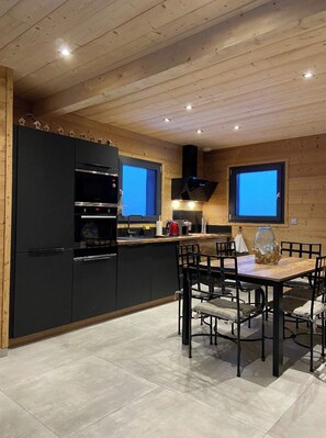 A modern kitchen with black cabinets, a dining table with chairs, and a large TV mounted on the wall. - Chalet "DIANA", at the foot of the ski slopes. Pets allowed  (Gérardmer)