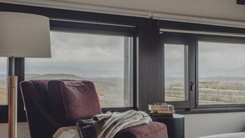 Una habitación con una ventana grande, una silla, una mesita de noche y una lámpara.