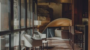 Un interior moderno con una pared de piedra, un techo curvo y una zona de bar con sillas de madera y una mesa blanca.