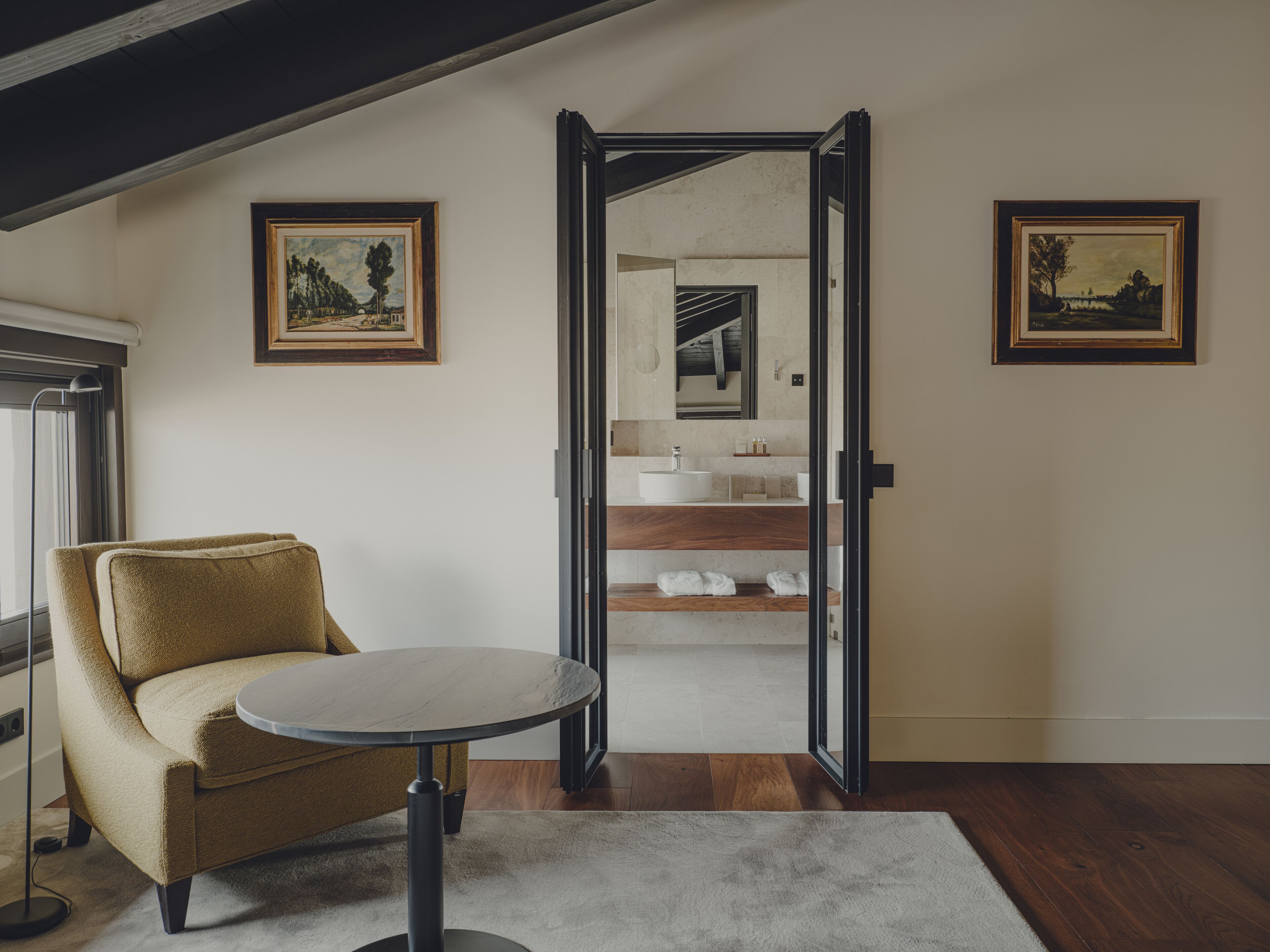 Una habitación moderna con sofá, una mesa redonda y vistas a un baño con lavabo y espejo.