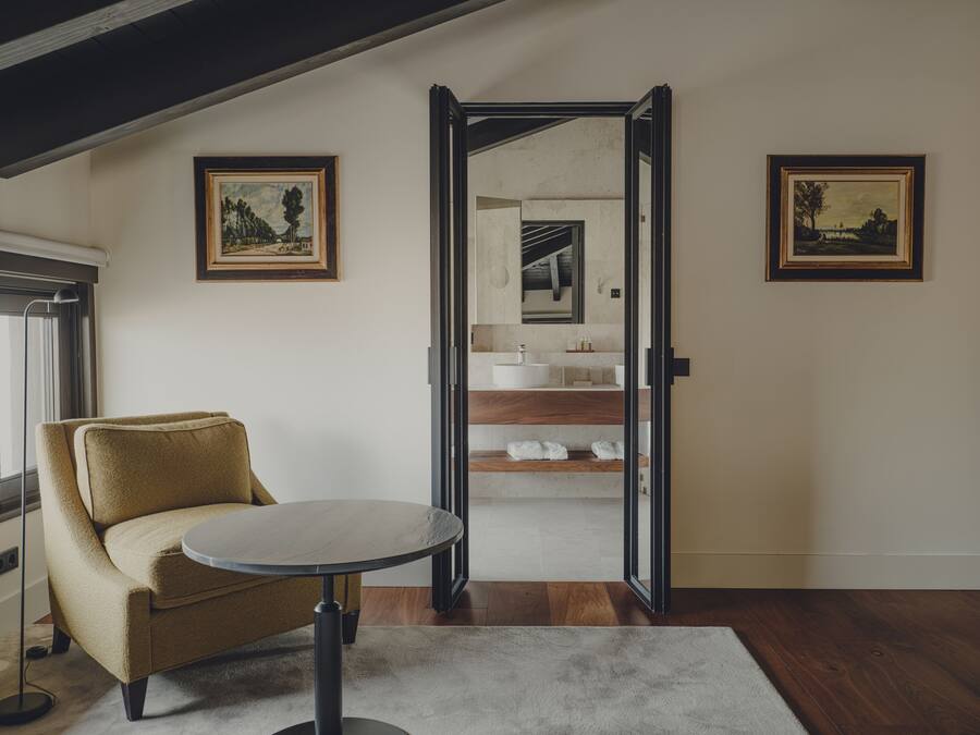 A modern room with a sofa, a round table, and a view into a bathroom with a sink and mirror.
