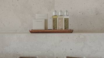A bathroom vanity with a marble countertop, a wooden tray holding a bottle of shampoo, a bottle of conditioner, and a bottle of body wash. There is a soap dish with a bar of soap and a small container below it.