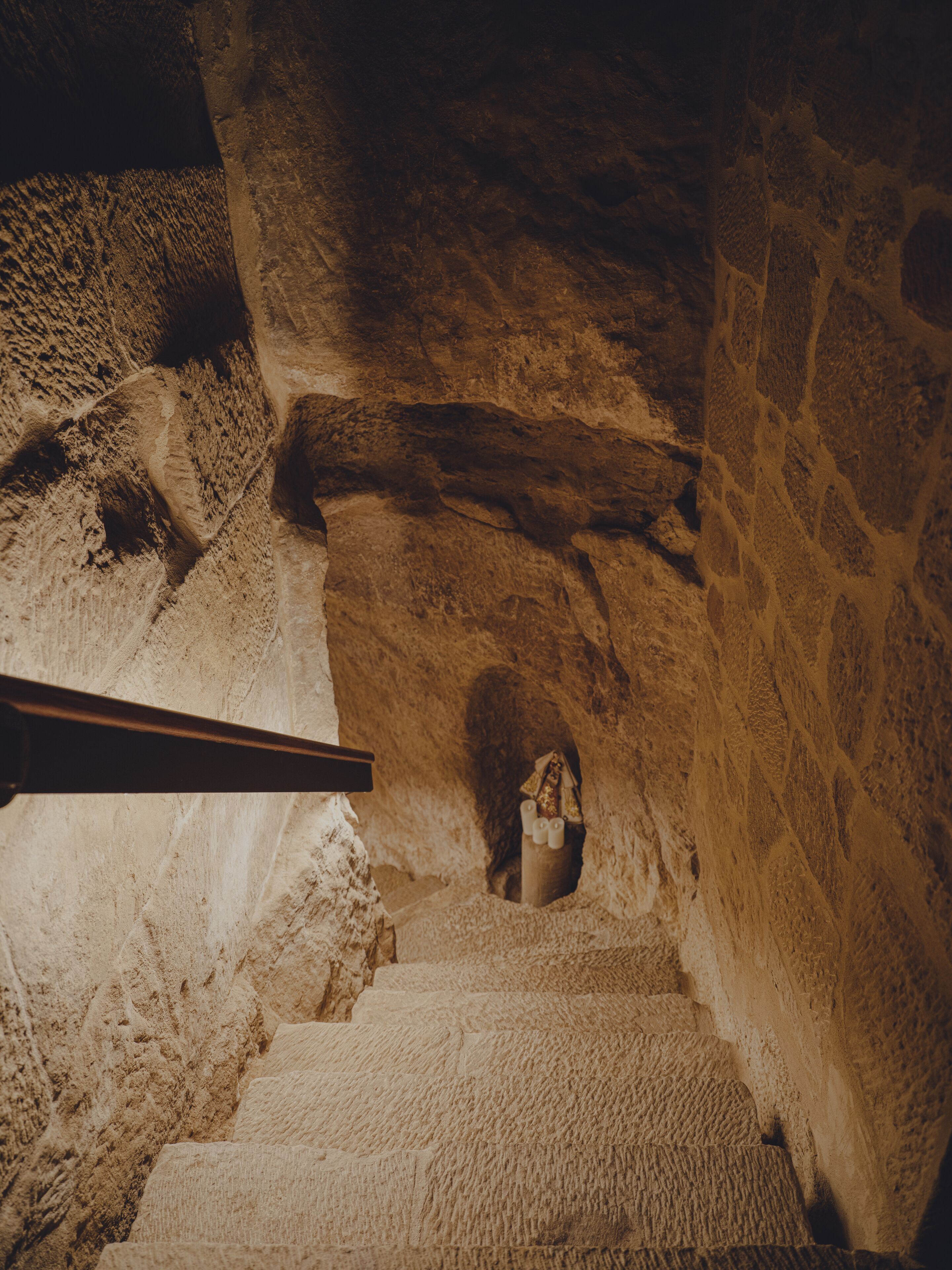 Una escalera de piedra con baranda de madera que lleva a una pequeña abertura en arco en la parte superior.