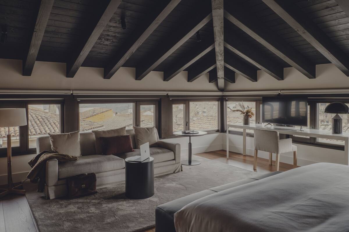 A modern bedroom with a loft-style ceiling, a large bed, a desk, and a sofa.