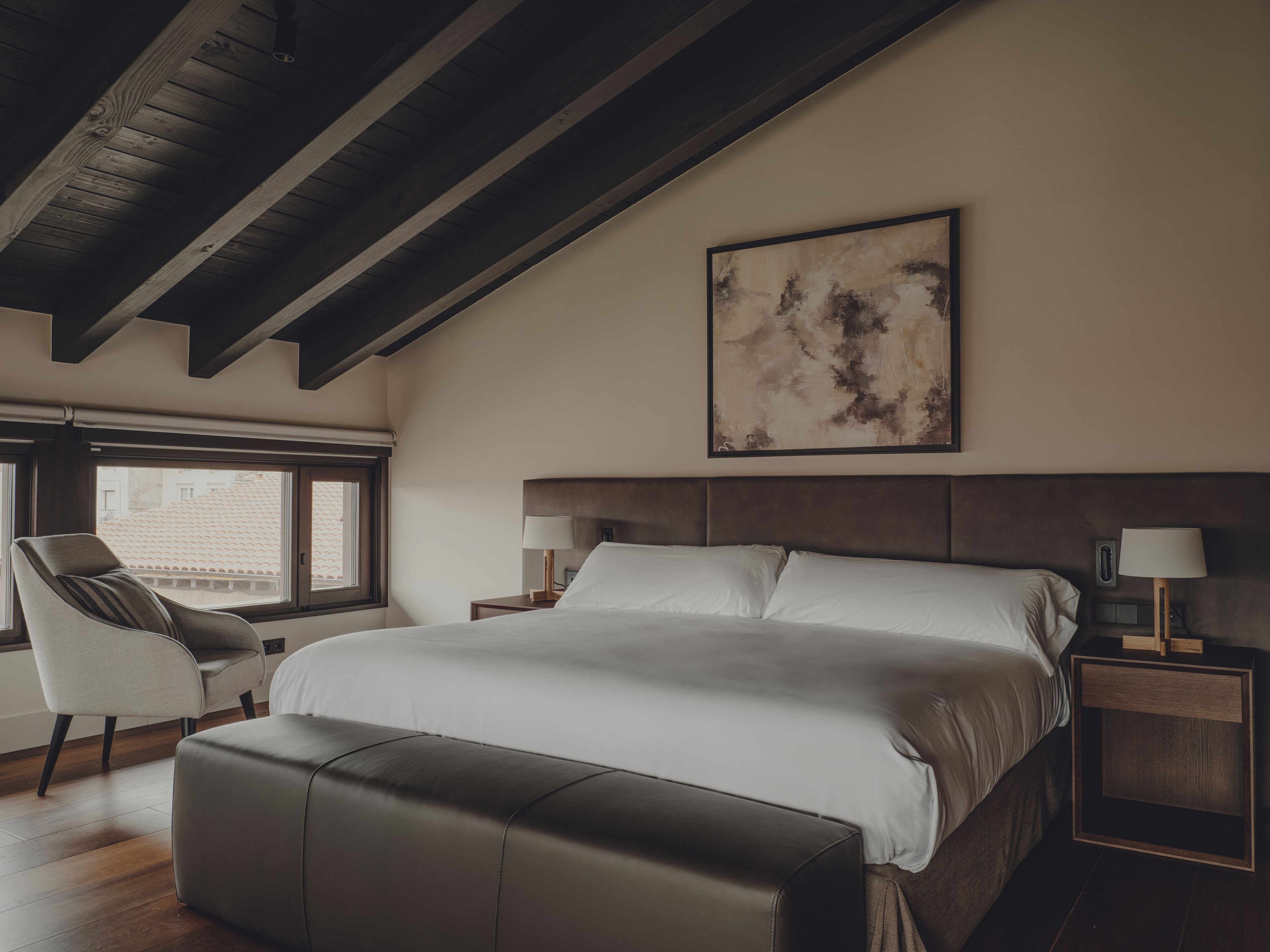 Un dormitorio con una cama grande, una silla, una mesita de noche y una ventana.